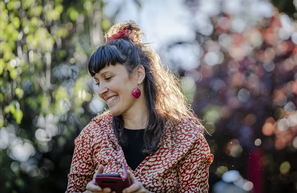 Eine Frau blickt lächelnd auf ihr Telefon